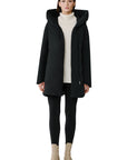 Woman wearing a black coat, white sweater, black leggings, and beige boots on a white background