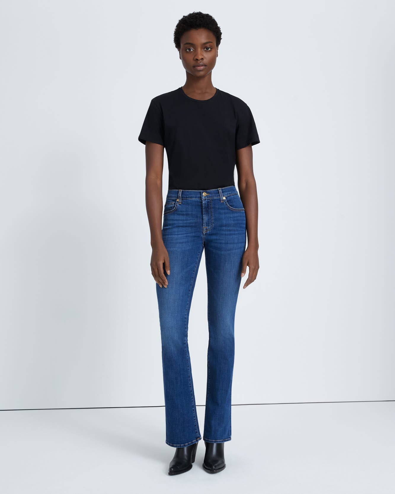 model wearing 7 for all mankind kimmie mid rise boot cut jean in duchess blue wash, paired with a black t-shirt and black boots