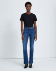 model wearing 7 for all mankind kimmie mid rise boot cut jean in duchess blue wash, paired with a black t-shirt and black boots