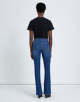 model wearing 7 for all mankind kimmie mid rise boot cut jean in duchess blue wash, paired with a black t-shirt and black boots, shown from the back