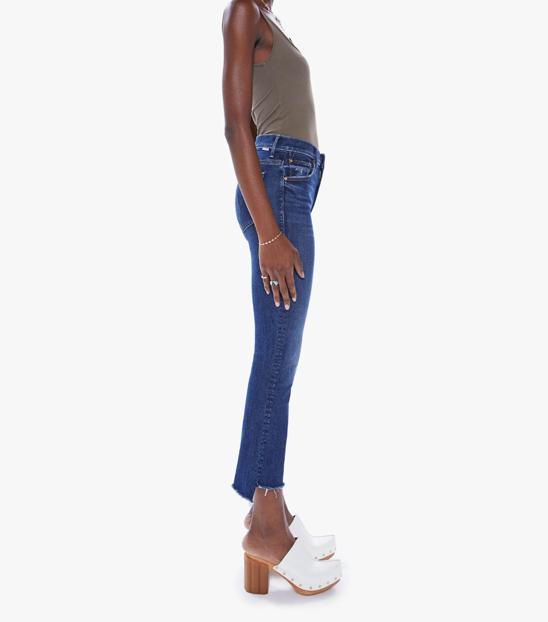 side view of the insider crop step fray jean from Mother in teaming up blue, styled with an olive green tank top and white clogs