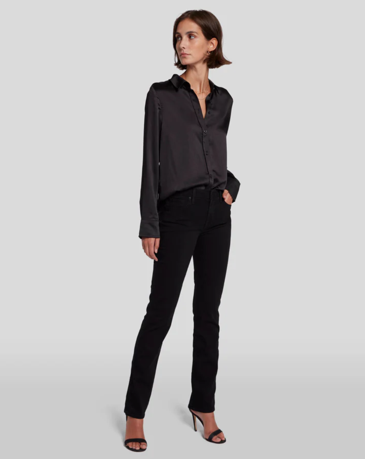 model standing at an angle wearing the 7 for all mankind kimmie mid rise straight in rinse black, paired with strappy sandals and black satiny blouse