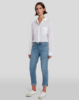 model wearing 7 for all mankind josefina boyfriend fit jean in bright light broken twill blue, paired with a white blouse and white sneakers