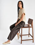 dark brown vegan leather ankle length wide leg trousers, styled with a beige shirt and model is seated