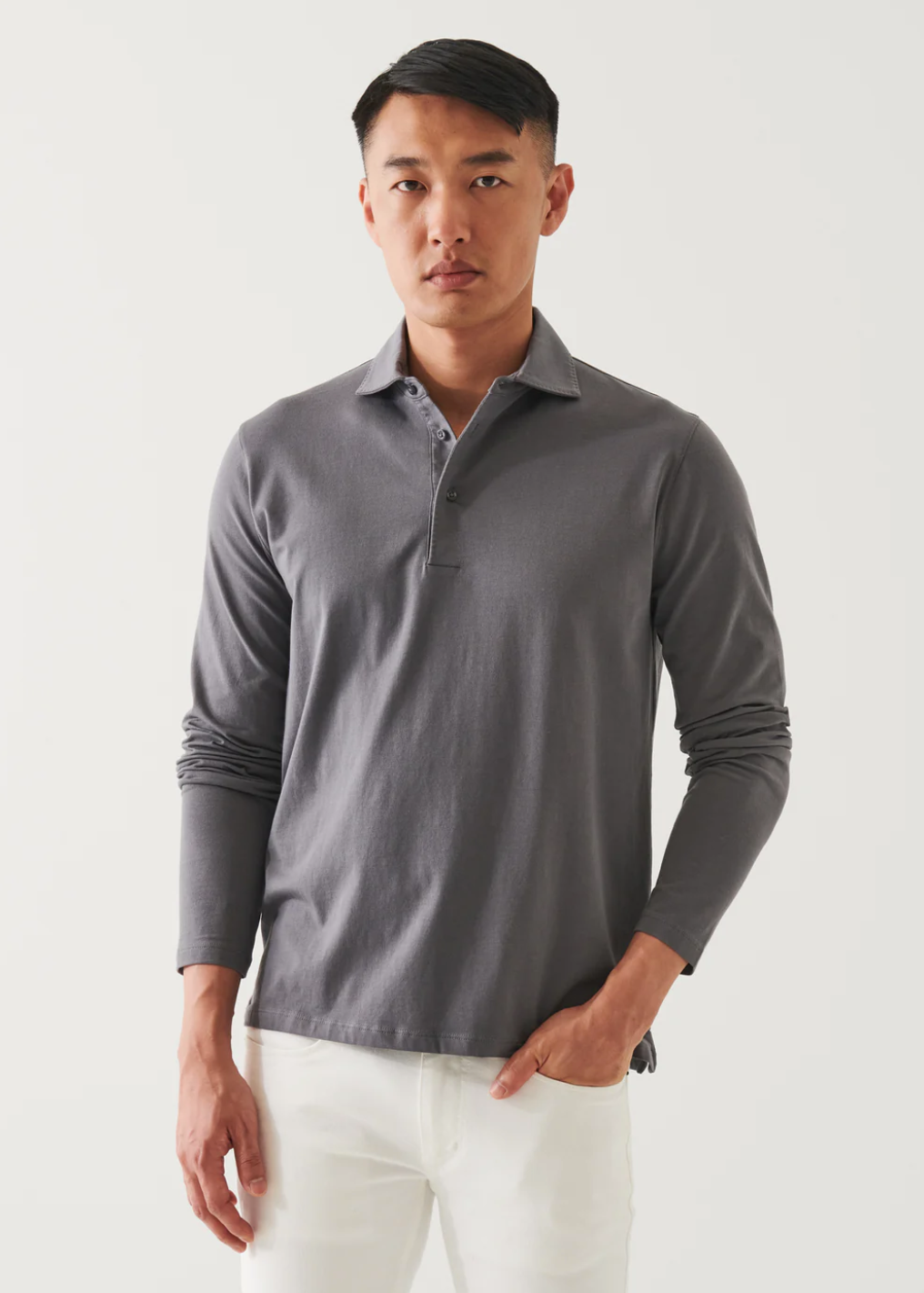 front view of the long sleeve pima stretch polo shirt in light grey, styled with white pants and model&#39;s hand in pocket