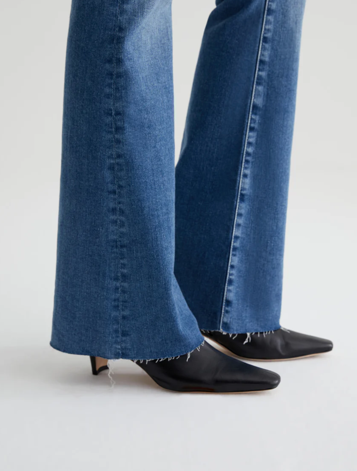 close up of the hem of ag jeans farrah boot cut jean in montecito blue, showing raw hem detail